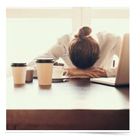 Woman with head down on desk among coffee cups.