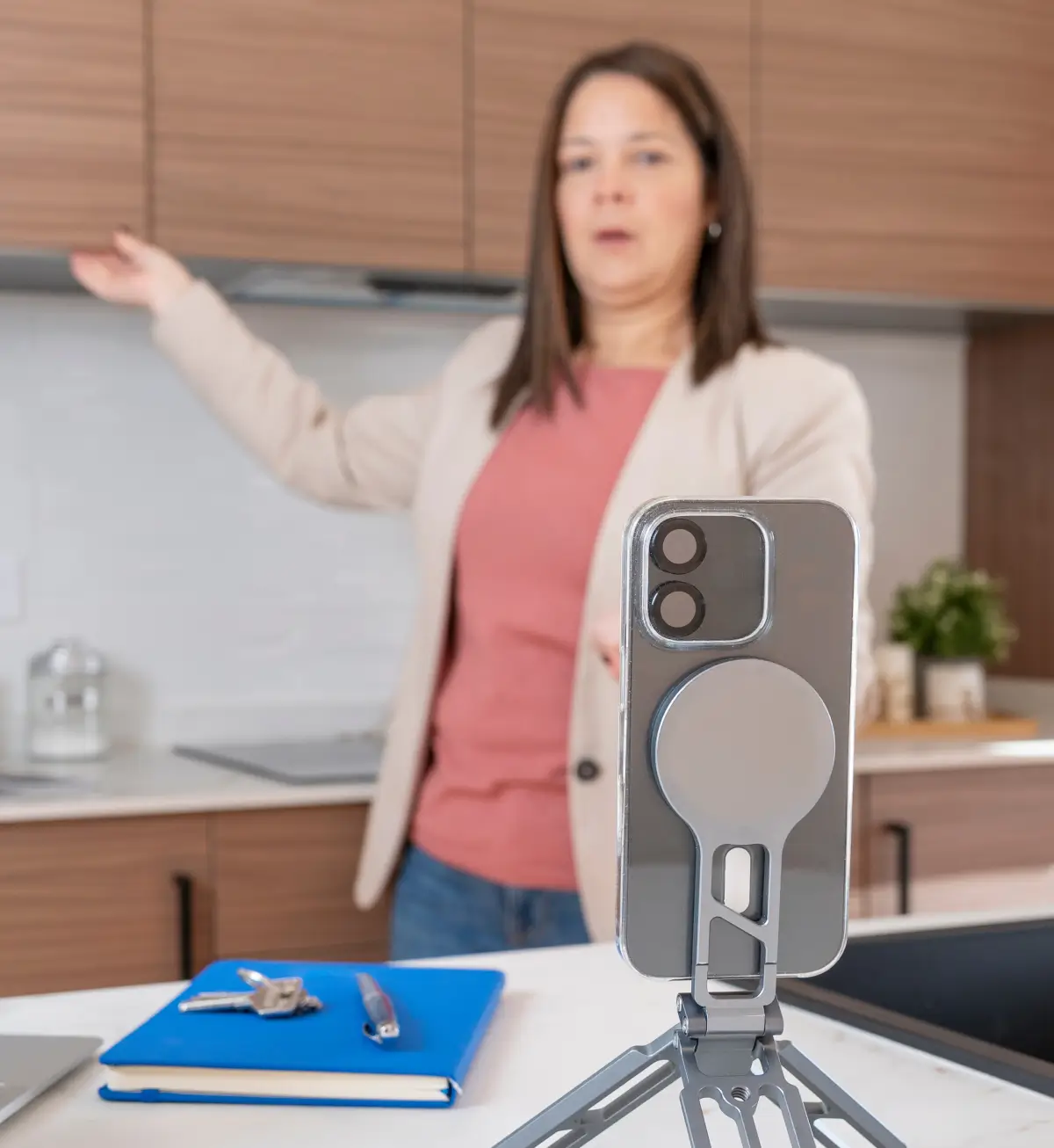 Real estate agent recording a property walkthrough video on a smartphone tripod in a modern kitchen.