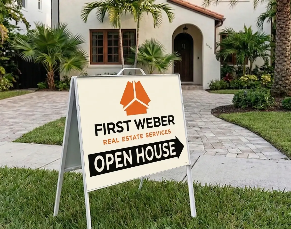 First Weber Real Estate Services open house A-frame sign in cream and black with an orange arrow displayed on a residential driveway