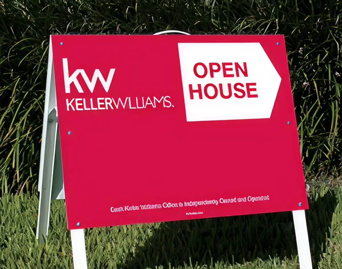 Keller Williams open house A-frame sign in red and white displayed outdoors against a green hedge