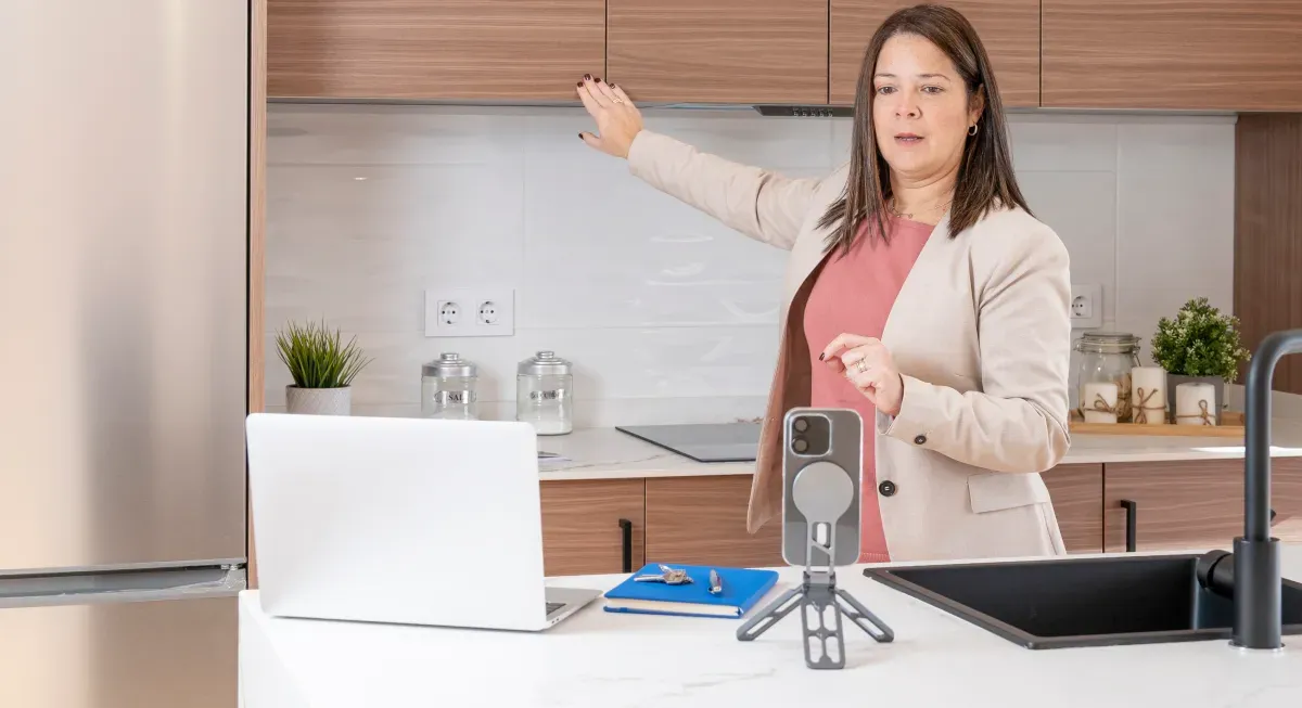 Realtor recording a property video tour on a smartphone in a modern kitchen.