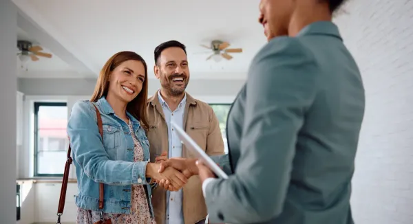 Real estate agent shaking hands with a smiling couple during a home showing.